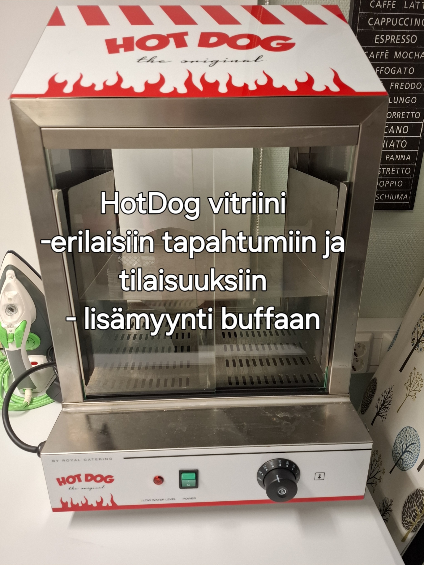Hot dog -lämpölaite, punainen liekkikuvioinen kansi ja lasiluukku, taustalla kahvitarjotin.